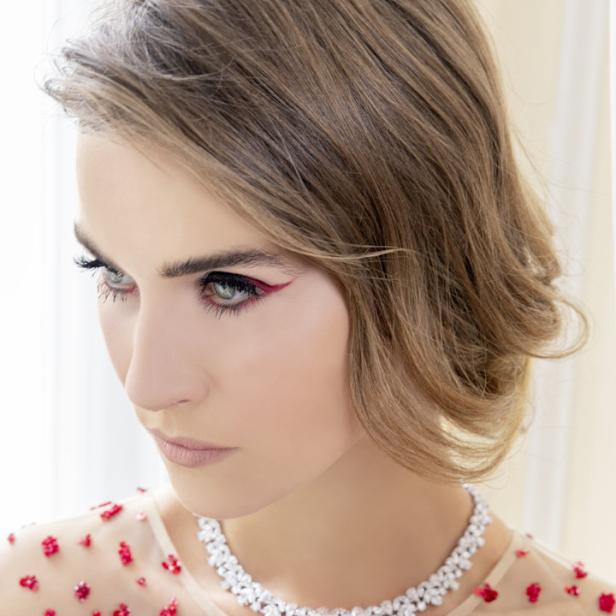 Eine Frau mit rotem Eyeliner und einer Halskette mit Blumenmuster blickt nach links.