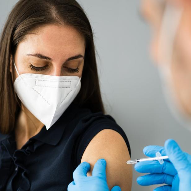 Eine Frau mit Maske erhält eine Impfung in den Oberarm von einem Arzt mit Handschuhen.