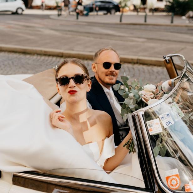 Ein Brautpaar fährt in einem Oldtimer-Cabriolet durch die Stadt.