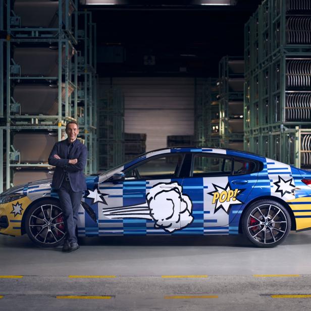 Ein Mann posiert vor einem BMW mit Pop-Art-Design in einer Lagerhalle.