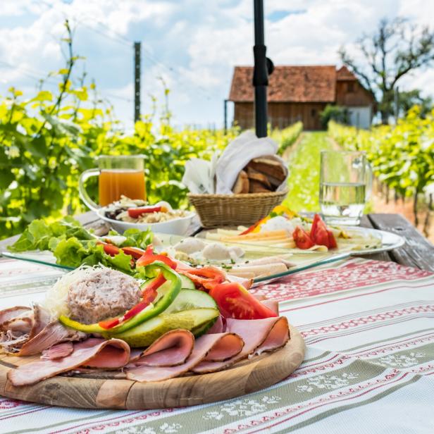 Eine Brettljause, eine kalte Platte mit Speisen, auf einem Holztisch im Weinberg.