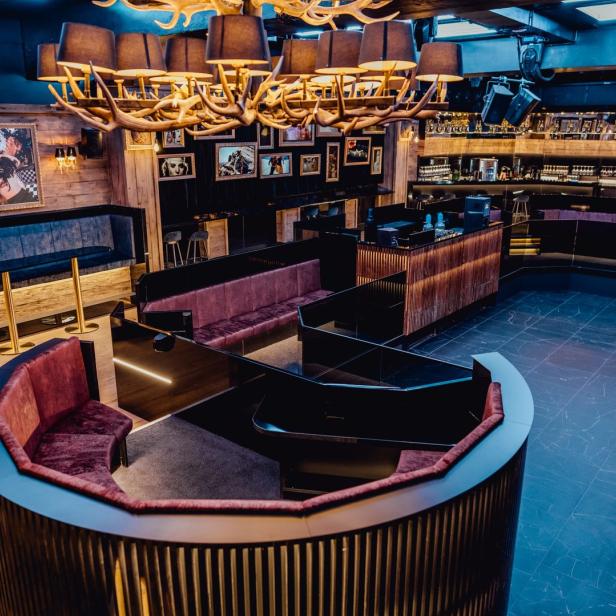 Innenansicht einer Bar oder eines Nachtclubs mit Sitzgelegenheiten und einer ungewöhnlichen Geweih-Lampe.