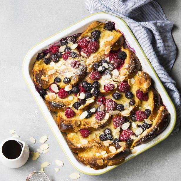 Ein Auflauf mit Brot, Himbeeren, Blaubeeren und Mandelsplittern, bestäubt mit Puderzucker.