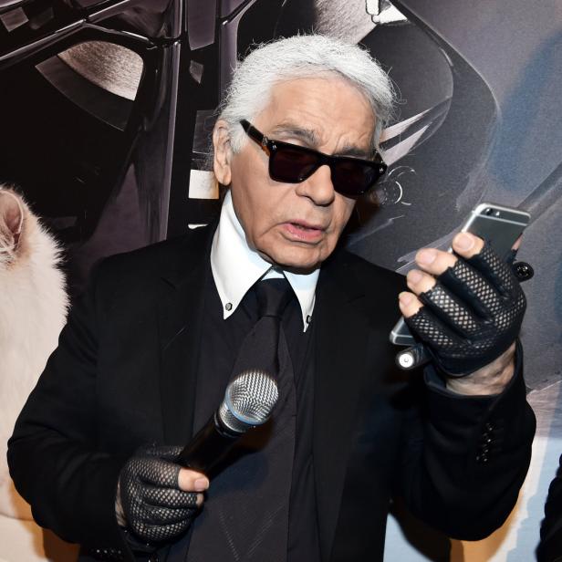 Karl Lagerfeld mit Mikrofon und Smartphone vor einem Bild seiner Katze Choupette.