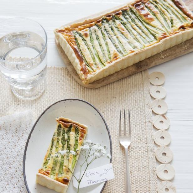 Ein Stück Spargelquiche mit einer Nachricht „Voor Mamma“ auf einem Teller.