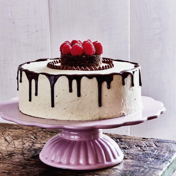Eine dekorierte Torte mit Schokoladenglasur und Himbeeren auf einem rosa Teller.
