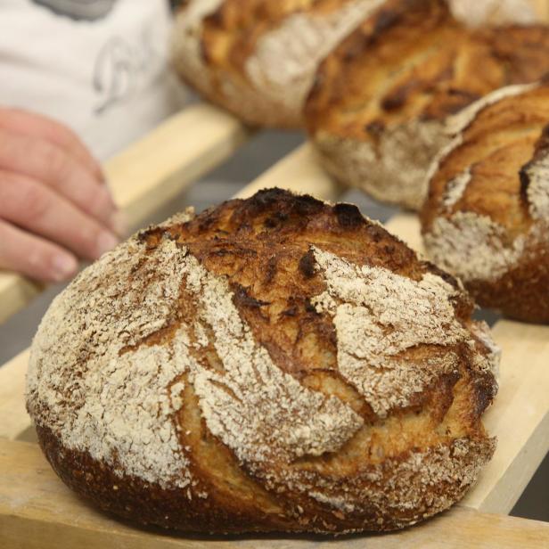 Mehrere Laibe frisch gebackenes Brot liegen auf einem Holzregal.