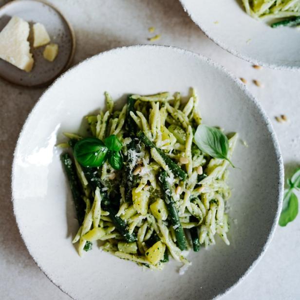 Zwei Teller Pasta mit Pesto, grünen Bohnen und Pinienkernen stehen auf einem Tisch.