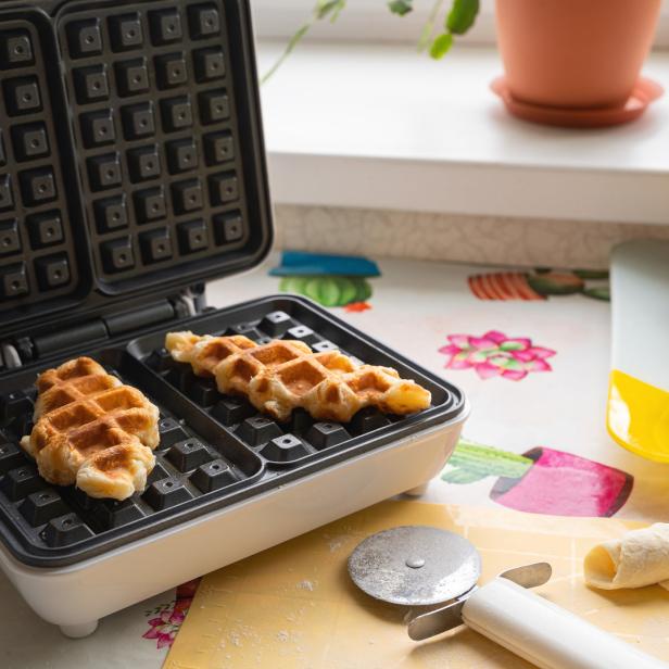 Ein geöffnetes Waffeleisen mit zwei fertigen Croffles darin.