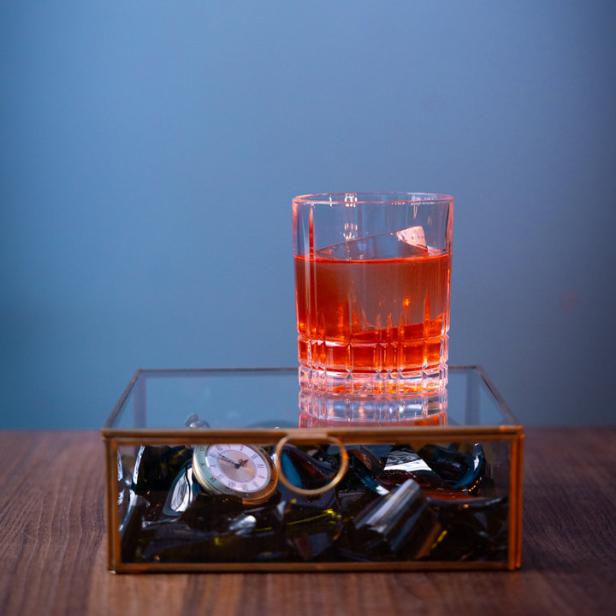 Ein Glas mit einem Getränk steht auf einer Schatulle mit einer Taschenuhr.