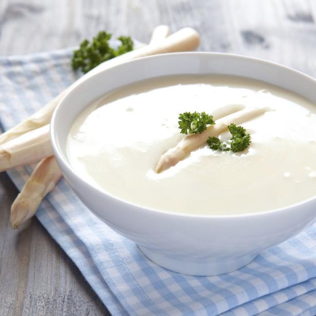 Eine Schüssel mit cremiger Spargelsuppe, garniert mit Petersilie.