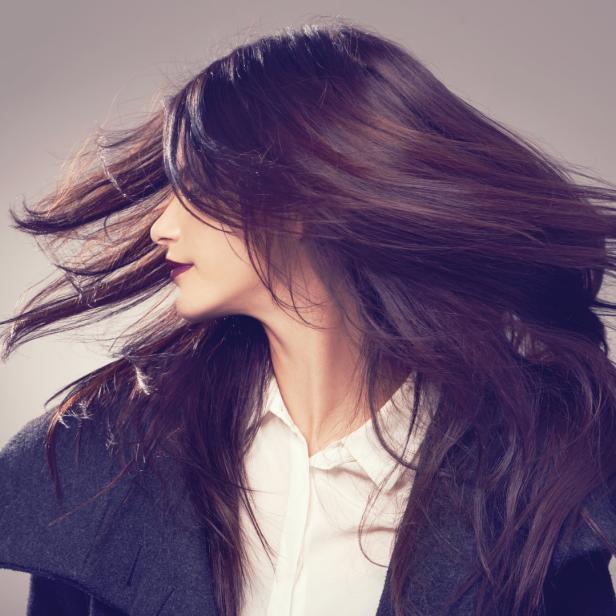 Eine Frau mit dunklen Haaren und dunklem Lippenstift, deren Haare im Wind wehen.