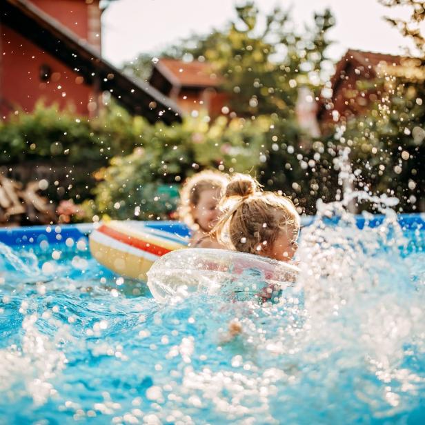 Zwei Kinder spielen mit Schwimmreifen in einem Pool voller spritzendem Wasser.