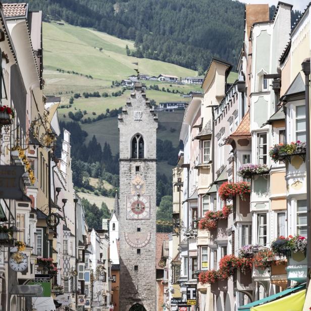 Blick auf den historischen Stadtturm von Sterzing, umgeben von bunten Häusern mit Blumenschmuck.