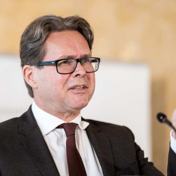 Ein Mann mit Brille und Anzug gestikuliert mit einem Stift in der Hand.