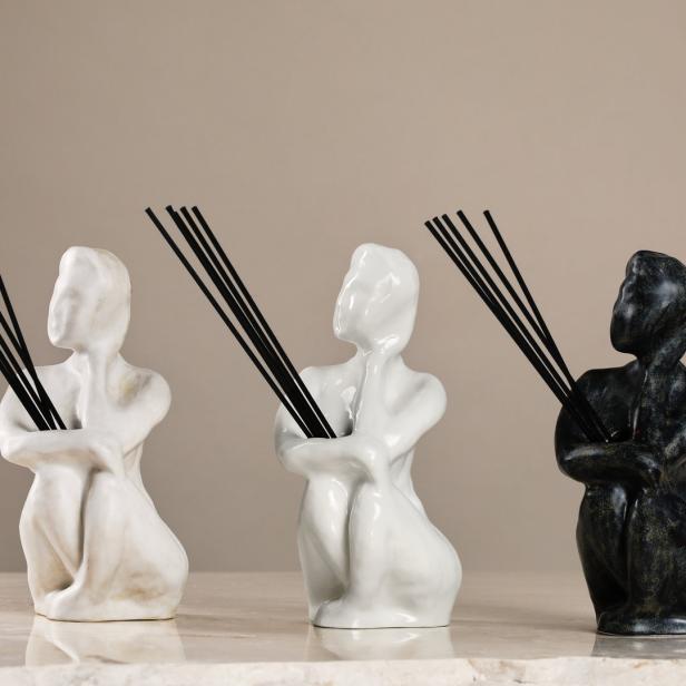 Drei Statuen in Form von sitzenden Figuren halten Duftstäbchen.