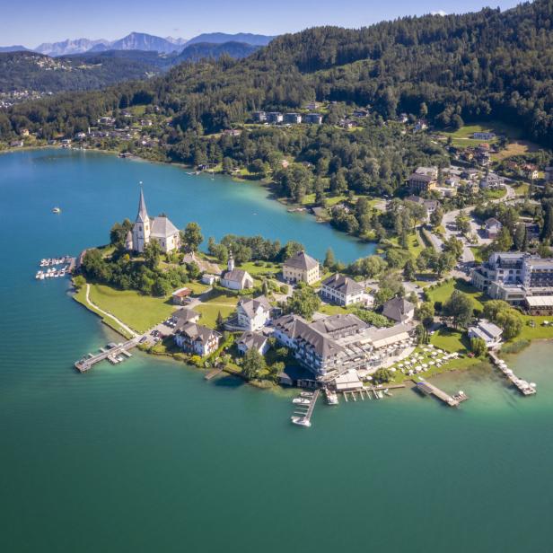 Luftaufnahme von Maria Wörth am Wörthersee mit Bergen im Hintergrund.