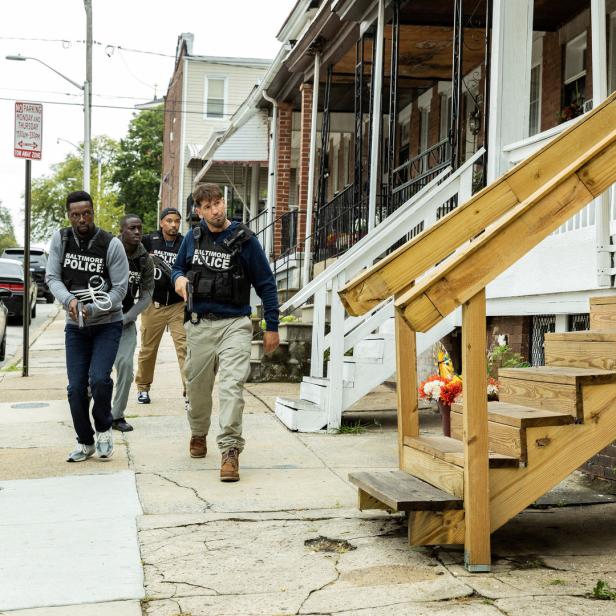 Mehrere Polizisten in kugelsicheren Westen mit der Aufschrift „Baltimore Police“ gehen auf einem Bürgersteig entlang.