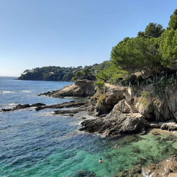 Blick auf eine felsige Küste mit klarem, türkisfarbenem Wasser und Badegästen.