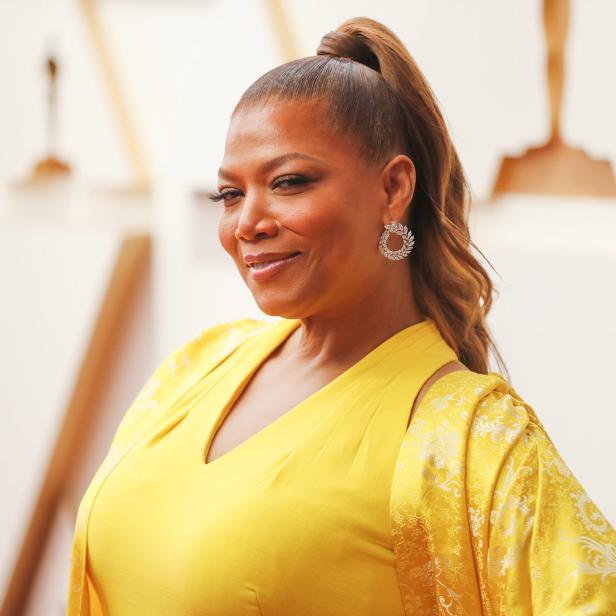 Queen Latifah in einem gelben Kleid mit hochgesteckten Haaren und Ohrringen.