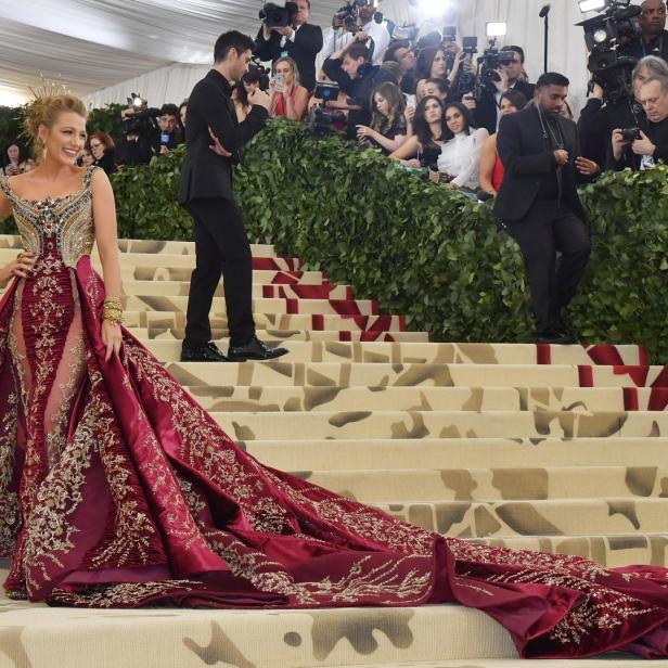 Blake Lively auf der Treppe der Met Gala in einem aufwendigen, burgunderroten Kleid mit langer Schleppe.