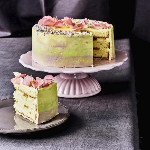 Ein angeschnittener, mit Blütenblättern dekorierter Kuchen auf einem rosa Teller und einem grauen Teller.