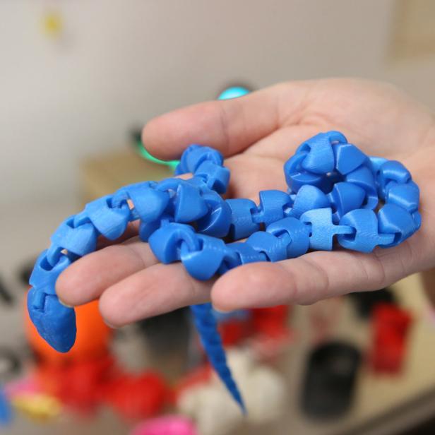 Eine Person hält eine blaue, flexible 3D-gedruckte Schlange in der Hand.