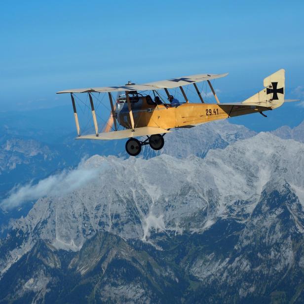 Ein historisches gelbes Flugzeug fliegt über eine Berglandschaft.