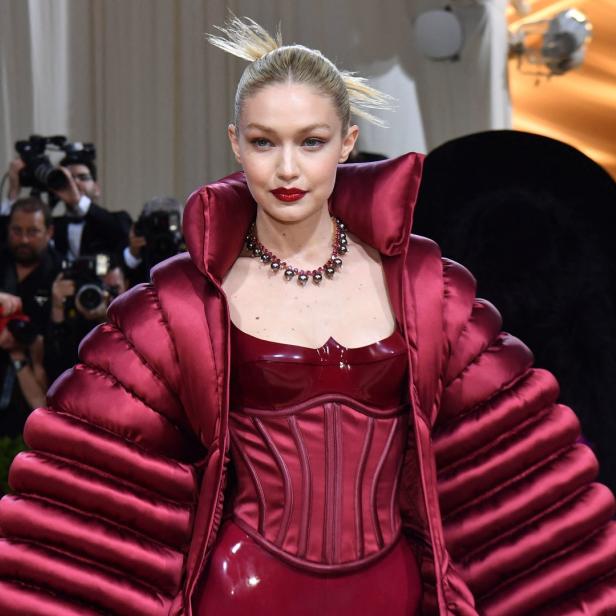 Gigi Hadid in einem roten Kleid und einer passenden Jacke auf dem roten Teppich.