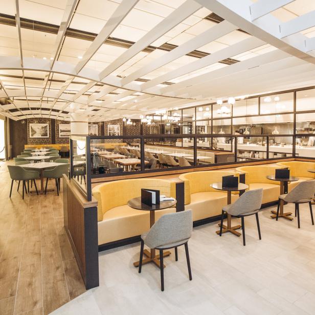 Innenansicht eines modernen Restaurants mit gelben Sitzbänken und grauen Stühlen.