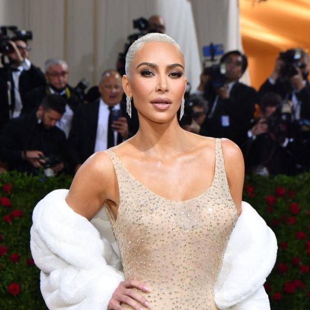 Kim Kardashian trägt ein mit Strass besetztes Kleid und eine weiße Pelzstola auf dem roten Teppich.