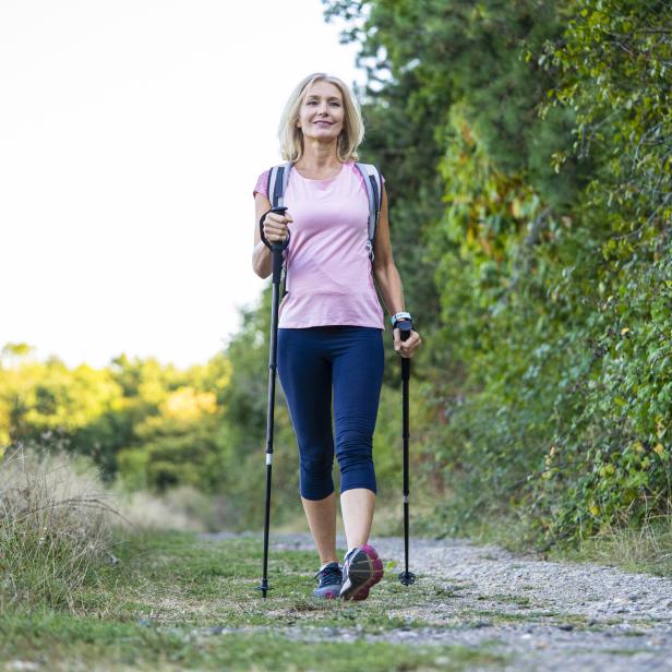 Eine Frau wandert mit Stöcken und Rucksack auf einem Waldweg.