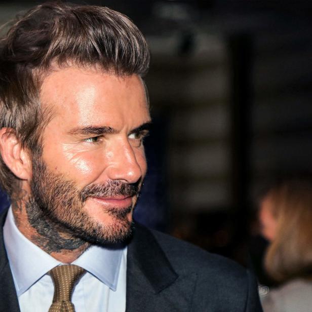 David Beckham im Anzug, mit Tätowierung am Hals, schaut zur Seite.