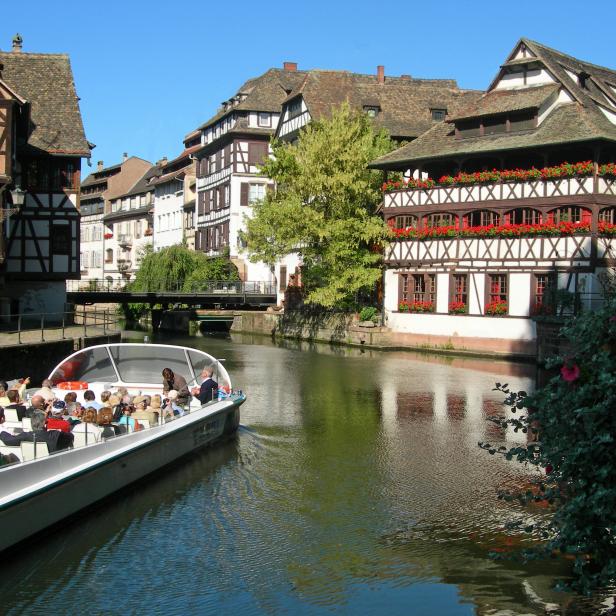 Ein Ausflugsboot fährt auf einem Kanal in Straßburg, umgeben von Fachwerkhäusern.
