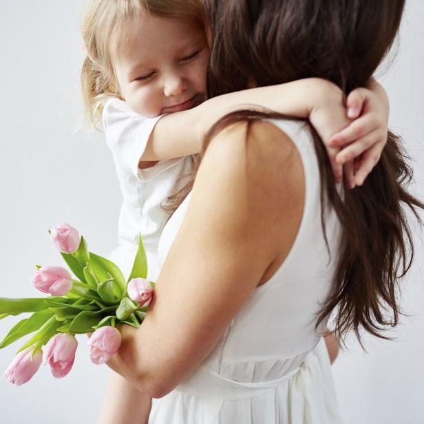 Eine Mutter hält ihre kleine Tochter im Arm, die einen Strauß rosa Tulpen umklammert.