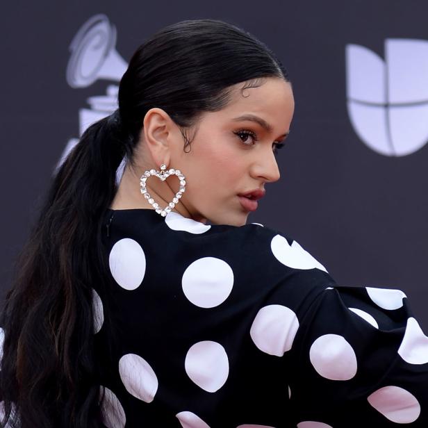 Rosalía trägt ein schwarz-weiß gepunktetes Kleid und herzförmige Ohrringe.