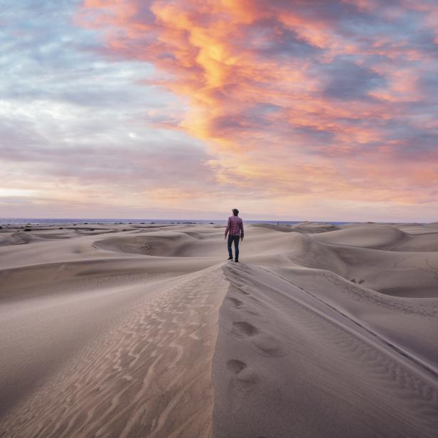 Ein Mann steht auf einer Sanddüne und blickt auf die Landschaft bei Sonnenuntergang.