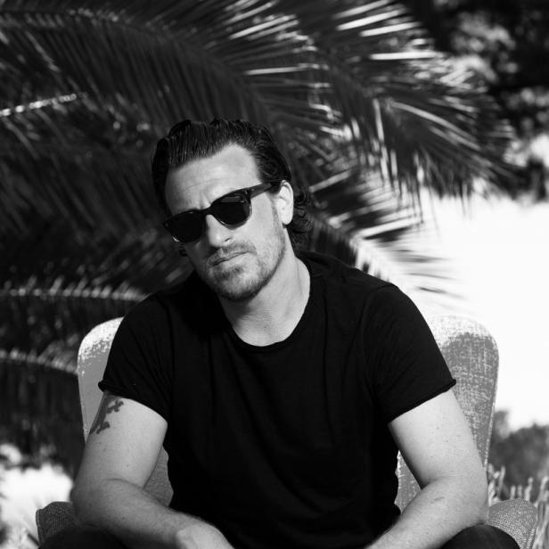Ein Mann mit Sonnenbrille sitzt in einem Sessel vor einer Palme.