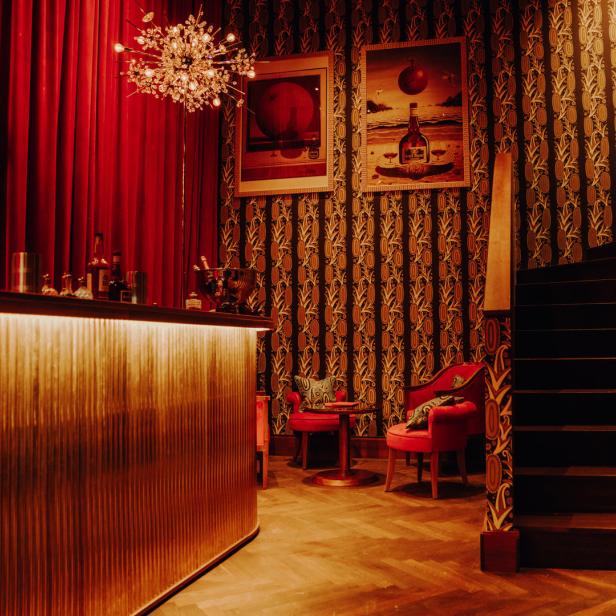 Eine Bar mit roten Samtvorhängen, gemusterter Tapete und einer Treppe.