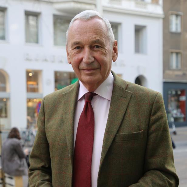 Ein älterer Mann im Tweed-Sakko hält eine blaue Gesichtsmaske in den Händen.