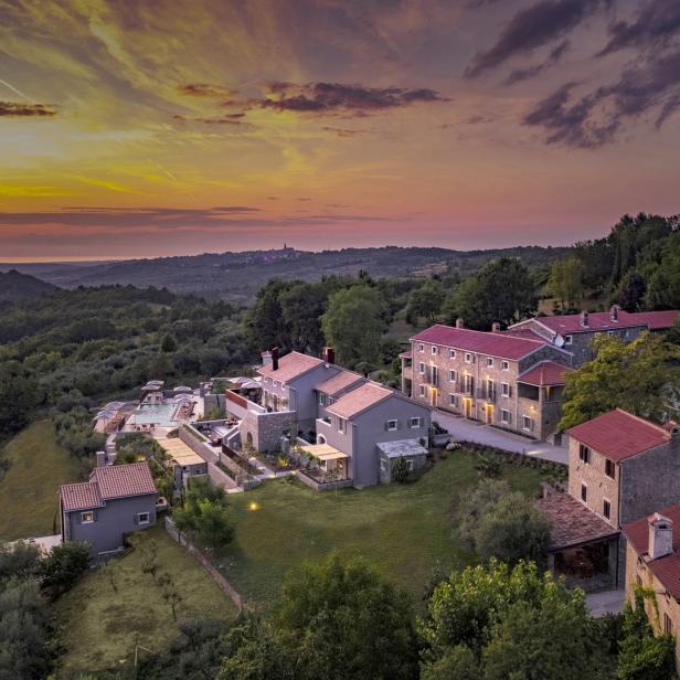 Luftaufnahme eines Resorts mit mehreren Gebäuden, einem Pool und üppigem Grün bei Sonnenuntergang.