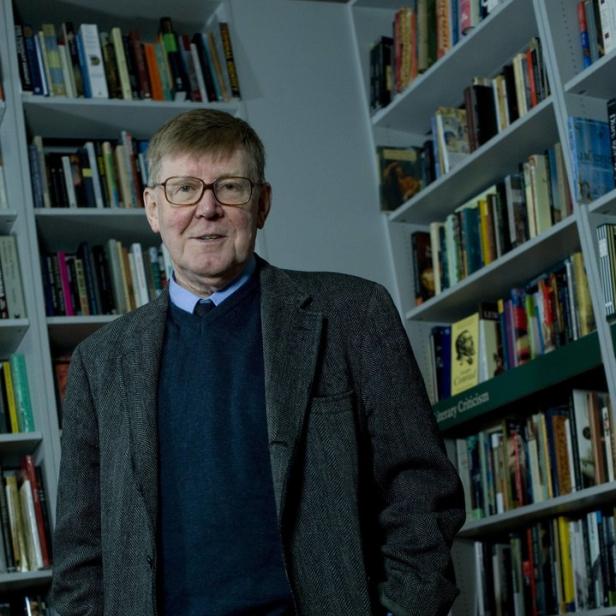 Ein Mann mit Brille und Jackett steht vor einem Bücherregal.