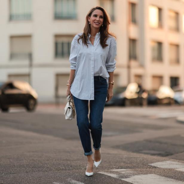 Eine Frau überquert in Jeans und Hemd eine Straße in der Stadt.