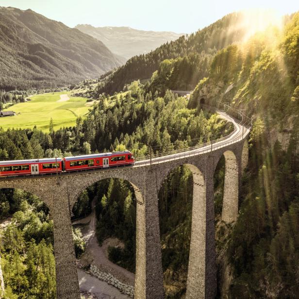 Ein roter Zug fährt über das berühmte Landwasserviadukt in der Schweiz.