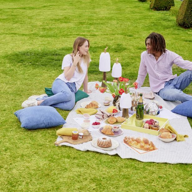 Ein Paar genießt ein Picknick mit Gebäck und Getränken auf einer Wiese.