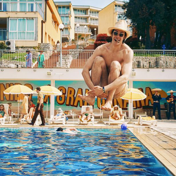 Ein Mann schwebt über einem Pool, während andere sich sonnen und eine Mariachi-Band spielt.