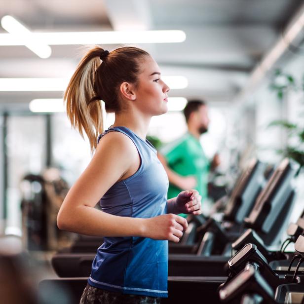 Eine junge Frau trainiert auf einem Laufband in einem Fitnessstudio.