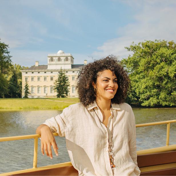 Eine Frau lächelt an der Reling eines Schiffes, im Hintergrund ein Schloss am See.