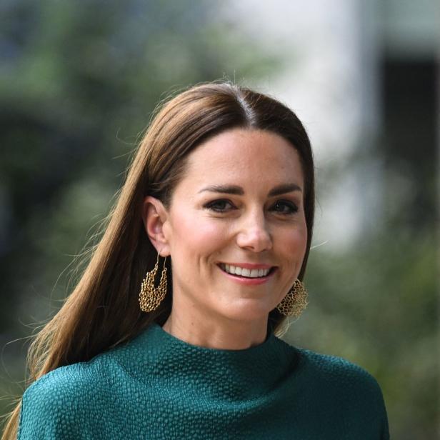 Catherine, Prinzessin von Wales, lächelt und trägt grüne Kleidung und goldene Ohrringe.