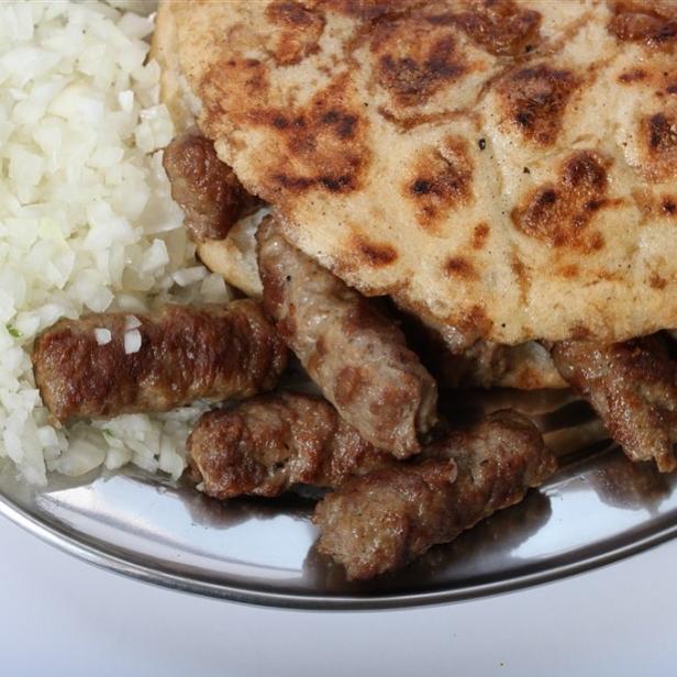 Ćevapi mit Fladenbrot und gehackten Zwiebeln auf einem Teller.
